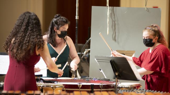  Three women percussion students playing together while wearing face masks.