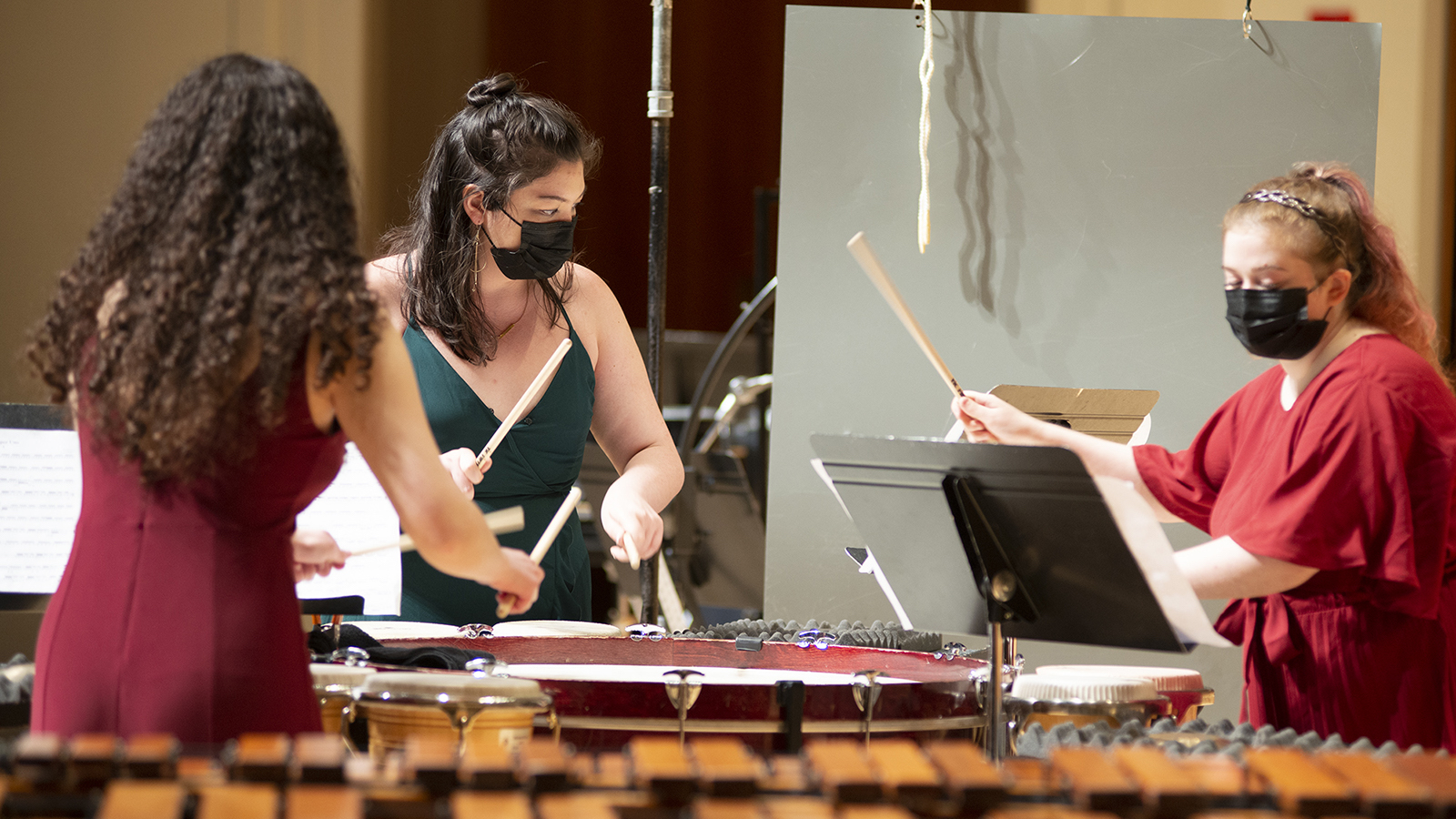  Three women percussion students playing together while wearing face masks.