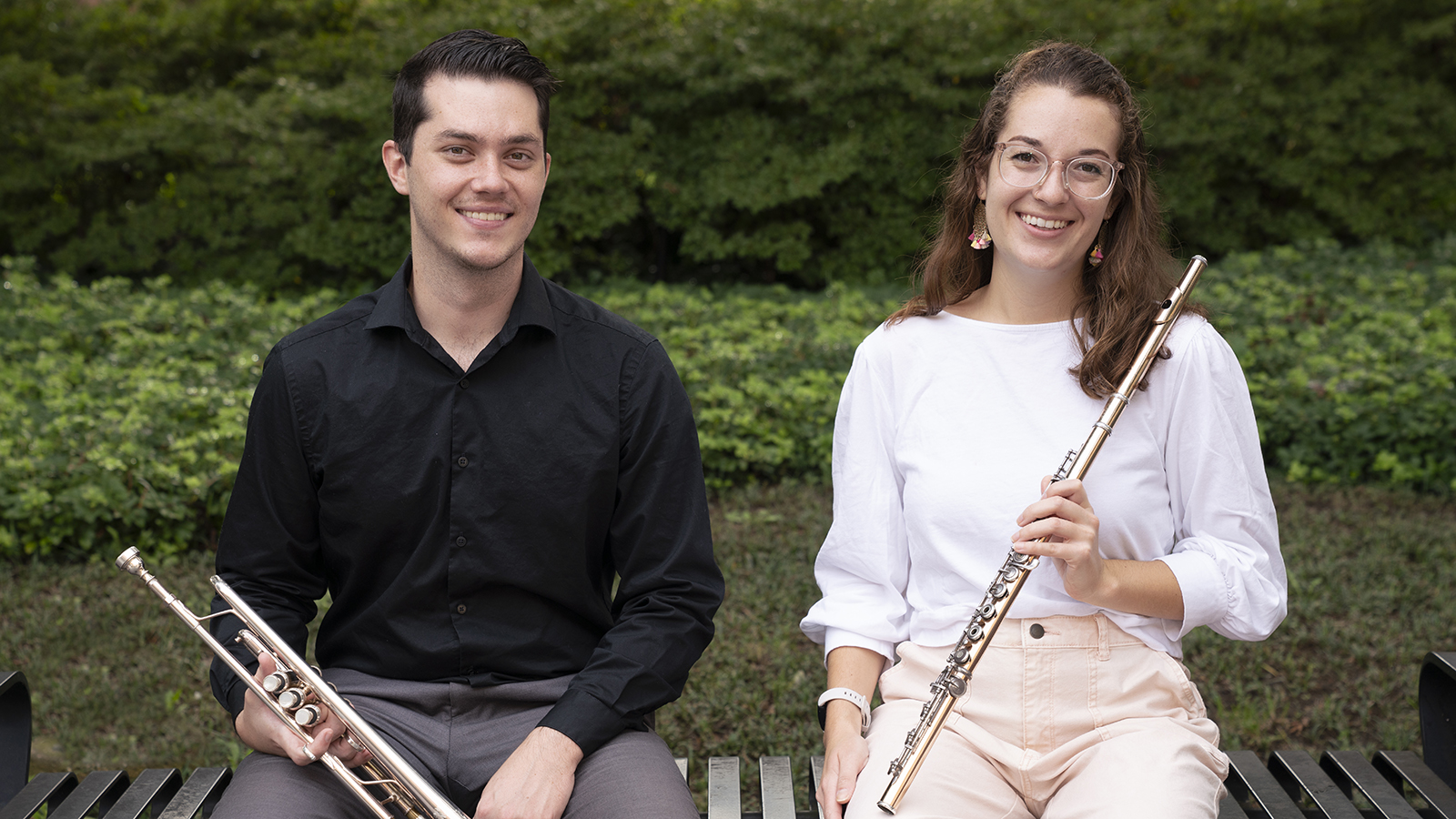 Dylan Rye and Jeanette-Marie Lewis are seated on a bench, holding their instruments.