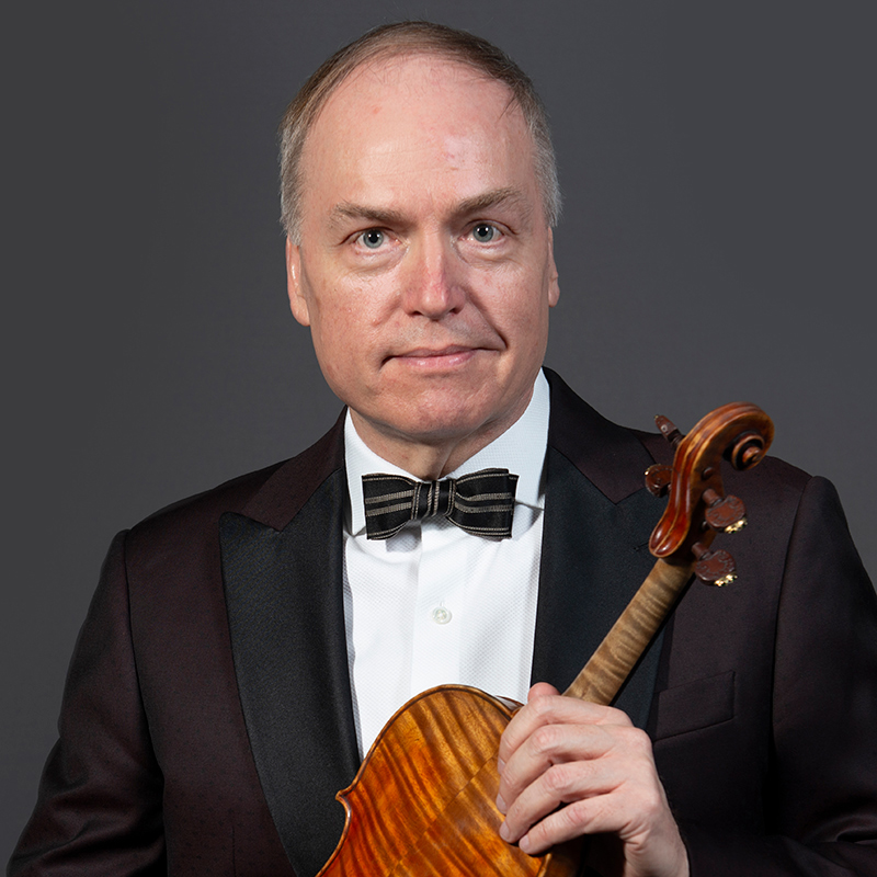School of Music faculty member David Salness. He is dressed in a tuxedo and is holding a violin against a grey backdrop.