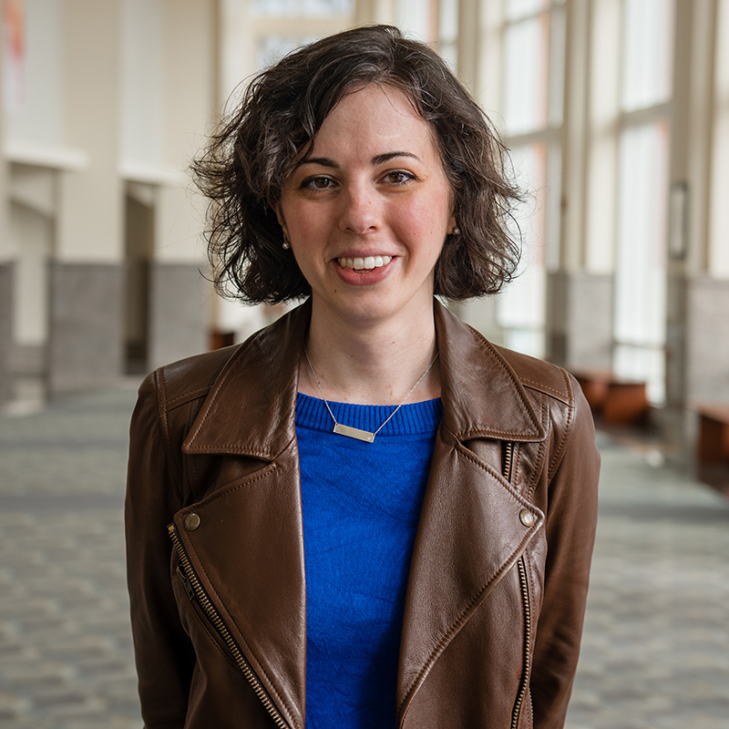 Assistant Professor Kelsey Klotz. She has short brown hair and is wearing a light brown leather coat over a blue shirt.