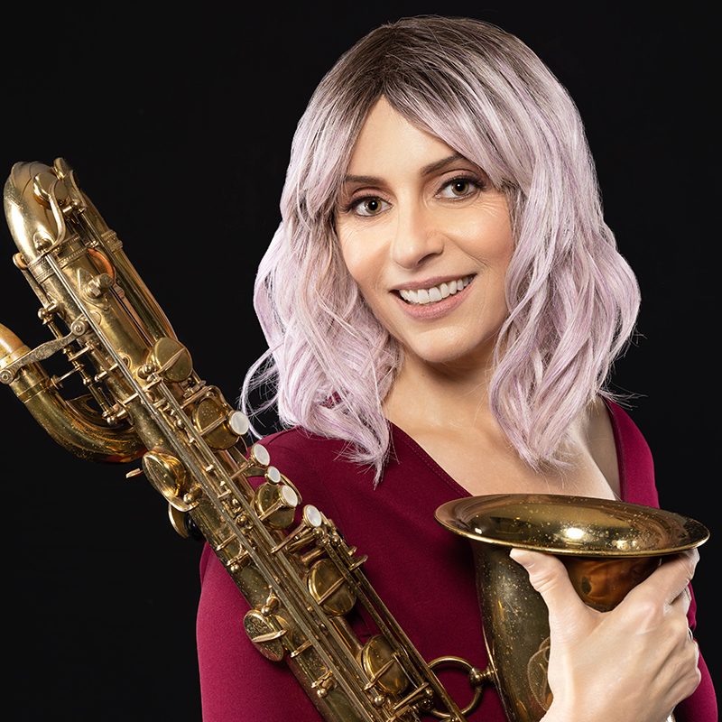 School of Music faculty member Leigh Pilzer. She is wearing a maroon dress and holding a saxophone against a black backdrop.