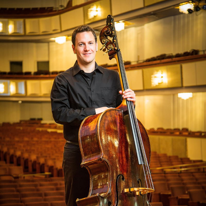 Double Bass Lecturer Paul Denola. He is wearing concert black and holding his double bass standing up.