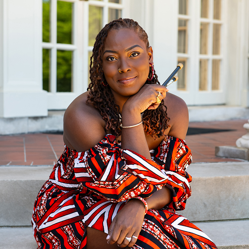 SOM Steelband Director Josanne Francis. She is wearing a red dress and holding steel pan mallets