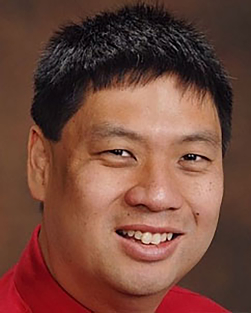 SOM Affiliate Faculty Eric Hung. He is wearing a red short against a brown backdrop.