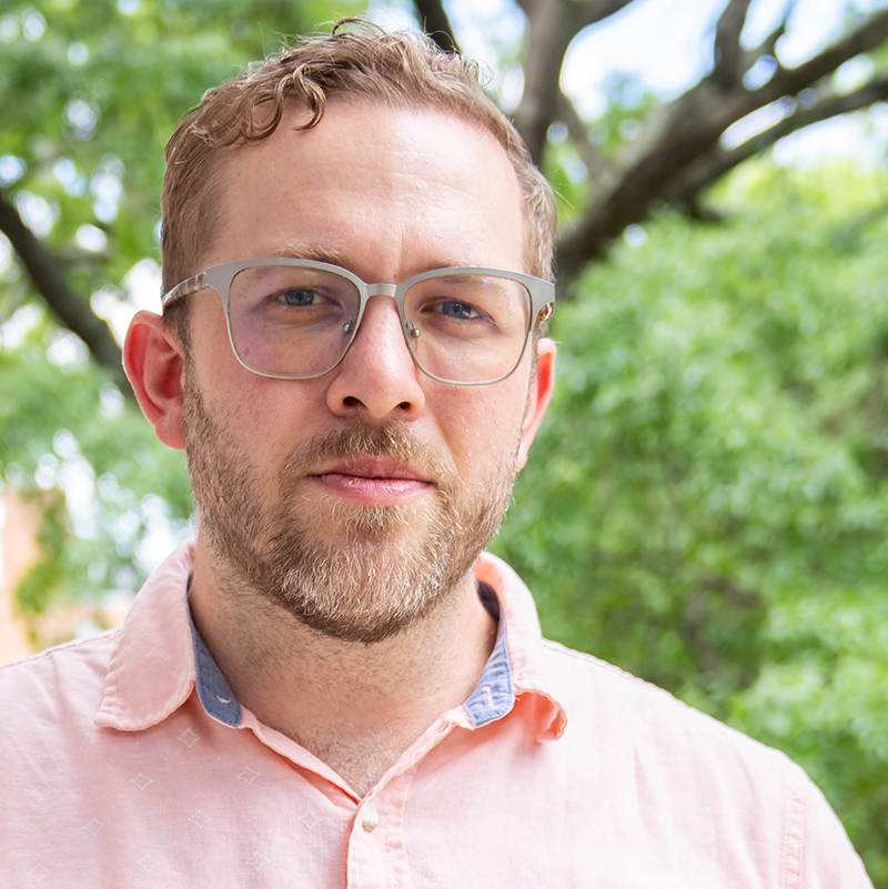 School of Music Faculty Brendan Kibbee. He is outside and wearing a red button-up shirt