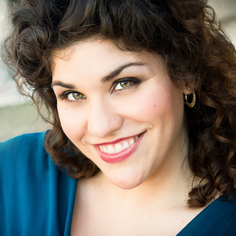 Assistant Artist in Residence Natalie Conte. She is wearing a deep blue shirt, dark curly hair and is smiling at the camera.