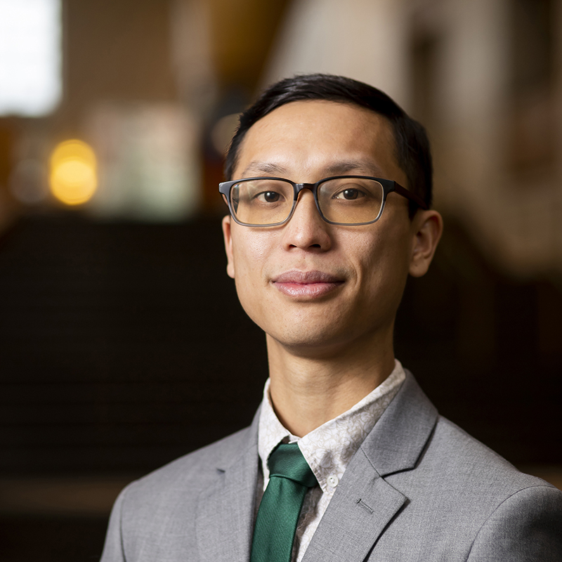 D.M.A. conducting student Trevor Tran. He is wearing a light gray suit with an emerald green tie.