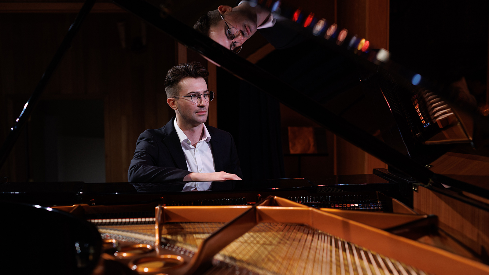 Jared Yoakem poses for a headshot at a piano. The image is taken through the lid of the piano, exposing the instruments strings.