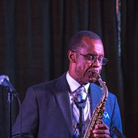 Charlie Young playing saxophone. He is wearing a navy blue suit.