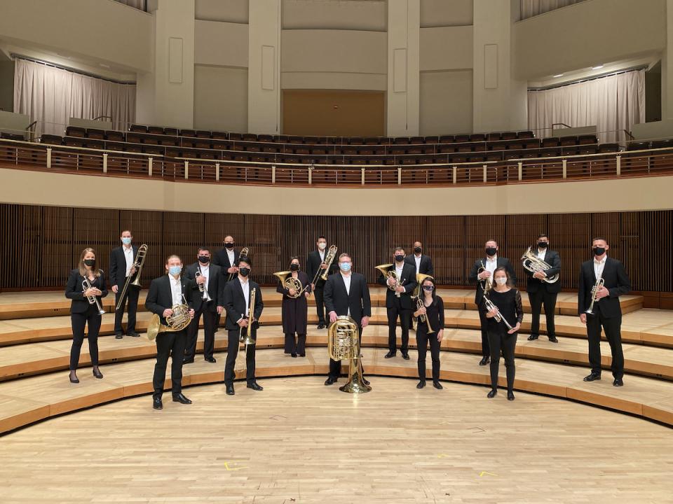  Members of Terrapin Brass stand on stage with members of the Barclay Brass. The musicians are all wearing concert black and holding their brass instruments.