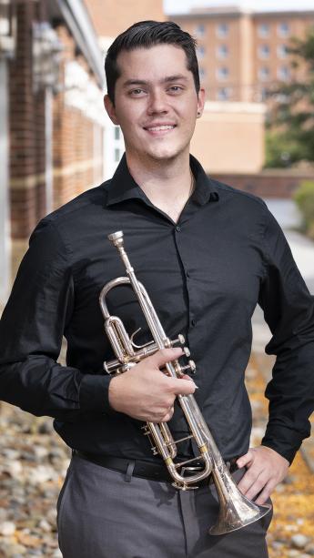 Dylan Rye, wearing a black dress shirt, poses for a photo with his trumpet.